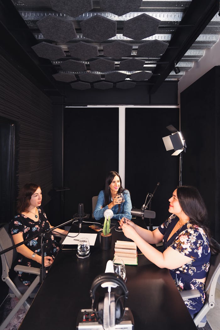 Three women recording a podcast indoors, showcasing a supportive environment with smiles and relaxed atmosphere.